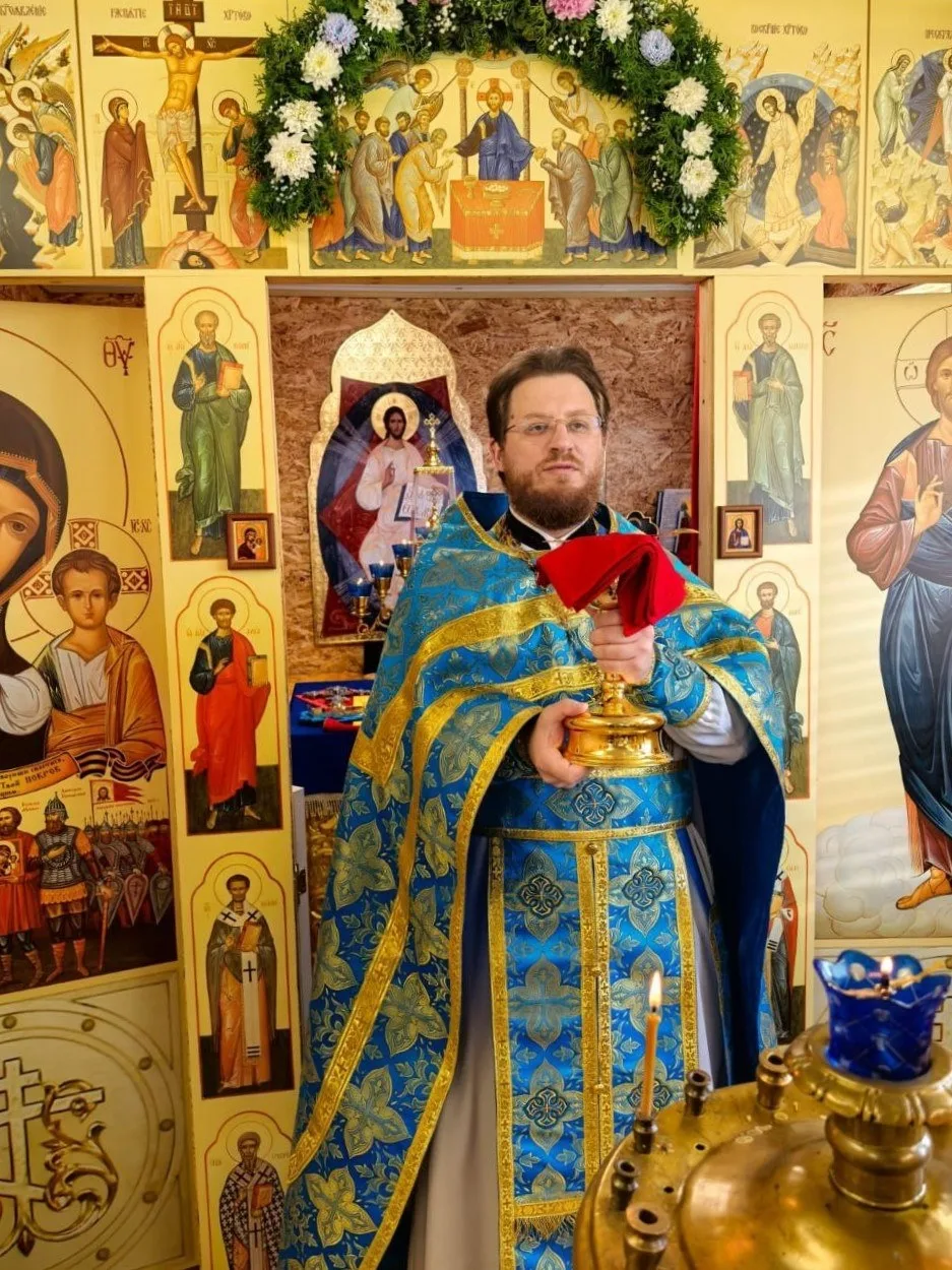 Священник в голубом облачении с кадилом на фоне временного иконостаса молитвенного дома