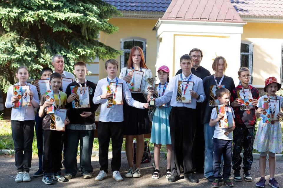 Группа детей с грамотами и медалями на улице у здания, двое детей держат кубок